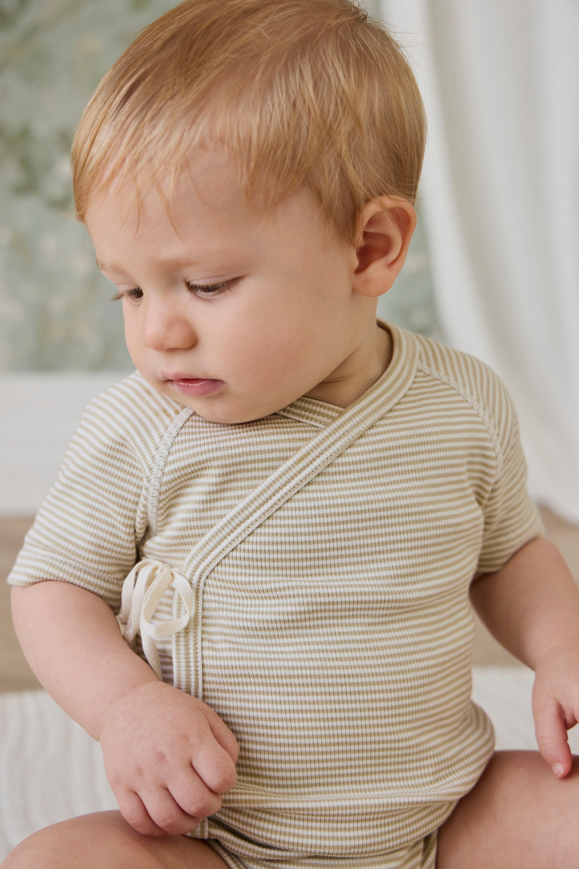 Combinaison courte bébé en coton côtelé fin à rayures crème et marron, avec ouverture cache-cœur et liens sur le côté pour le confort quotidien